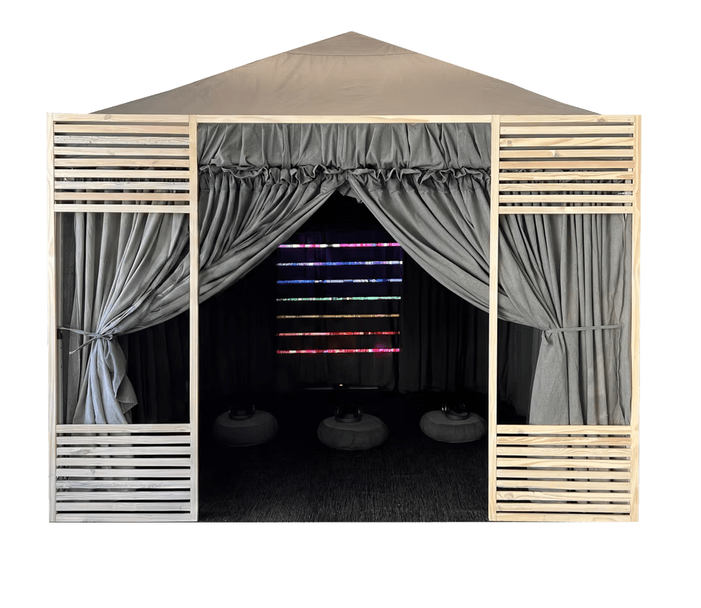 Chakra Meditation Booth with a wooden frame, gray curtains, seating cushions, and horizontal bands of colored LED light inside.