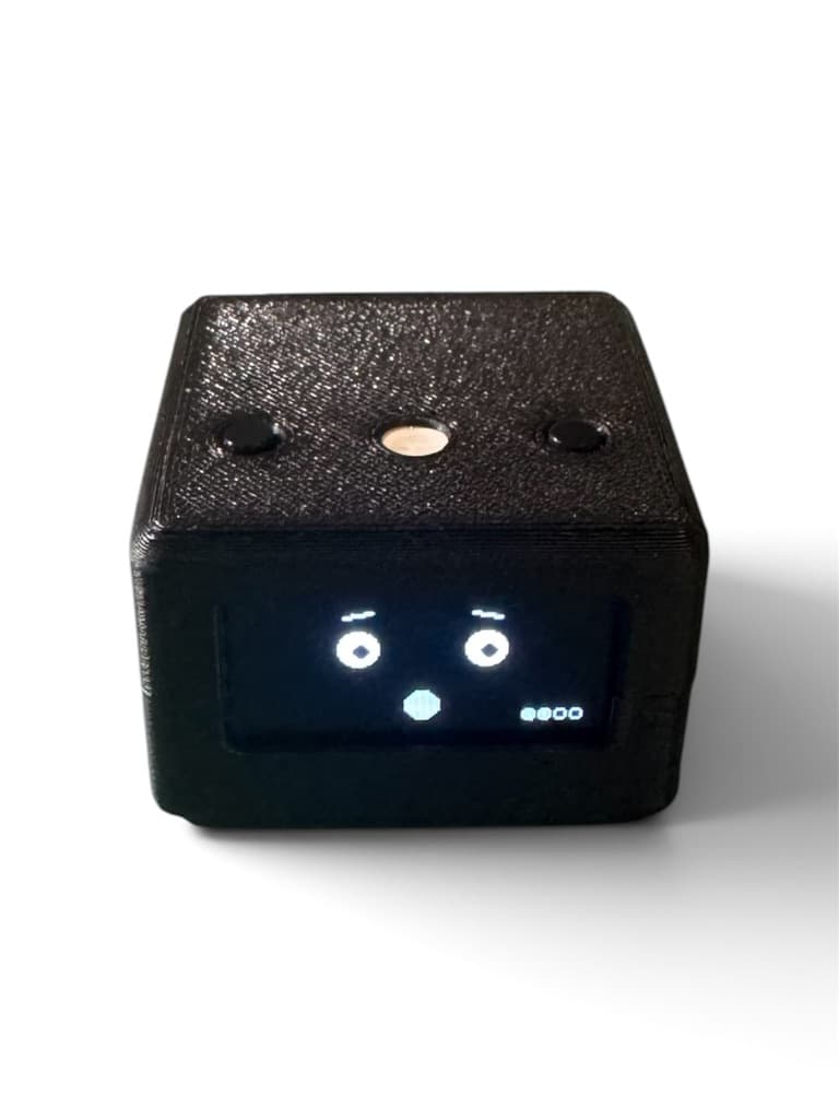 Cubelet, a black desktop device with an expressive pixel face on its screen, two top buttons, and a central LED.